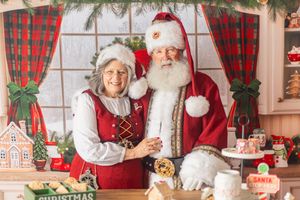 Santa Claus and Mrs. Claus smiling together in a festive Christmas workshop with holiday decorations.