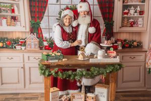 Santa and Mrs. Claus baking together in a festively decorated Christmas kitchen with gingerbread houses and holiday decor.