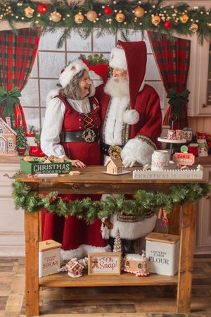 Santa and Mrs. Claus share a joyful moment at a festive cookie-baking table decorated with Christmas garland.
