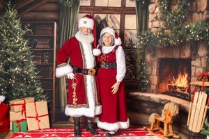 Santa Claus and Mrs. Claus pose together in festive red costumes beside a decorated Christmas tree and fireplace.