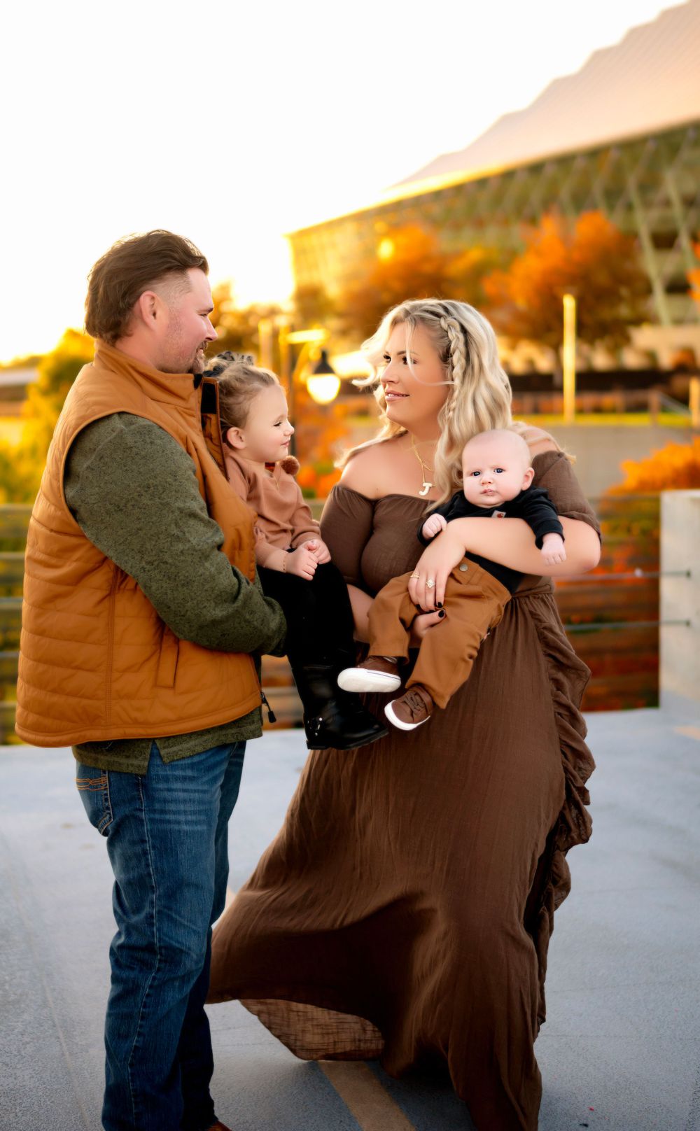 Family in coordinating brown and tan outfits share a joyful moment together during golden hour sunset outdoors.