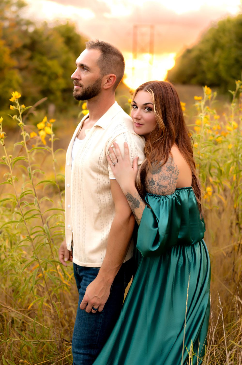 A couple poses in a wildflower field at sunset, with the woman in a teal dress and the man in cream colored shirt.