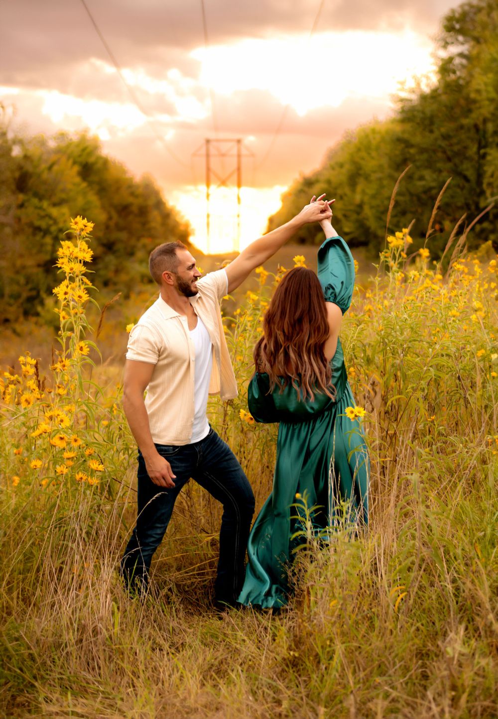 A couple dances together in a wildflower field at sunset with power lines and trees silhouetted in the background.