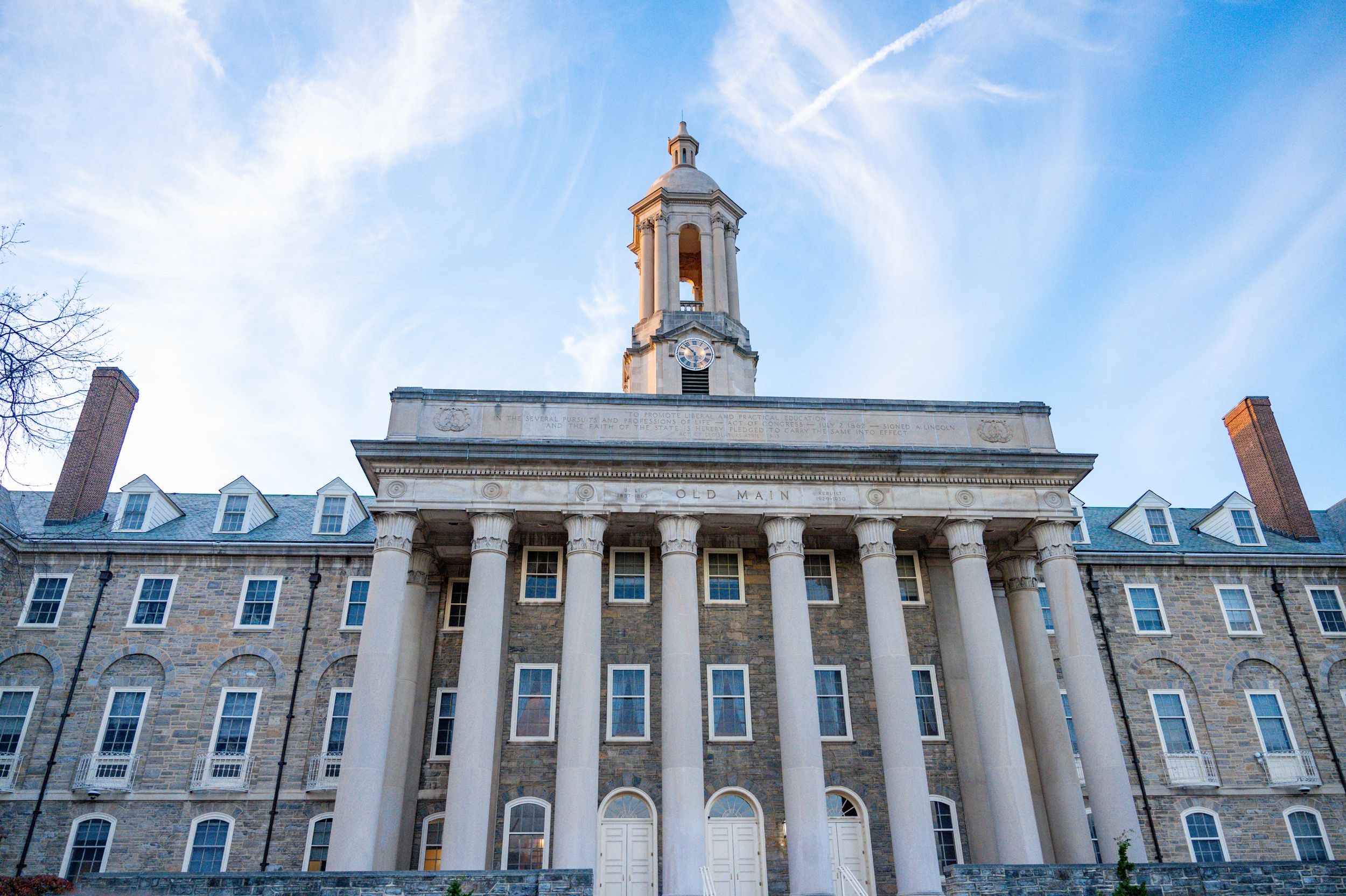 Neoclassical college building with tall white columns and bell tower against blue sky.
