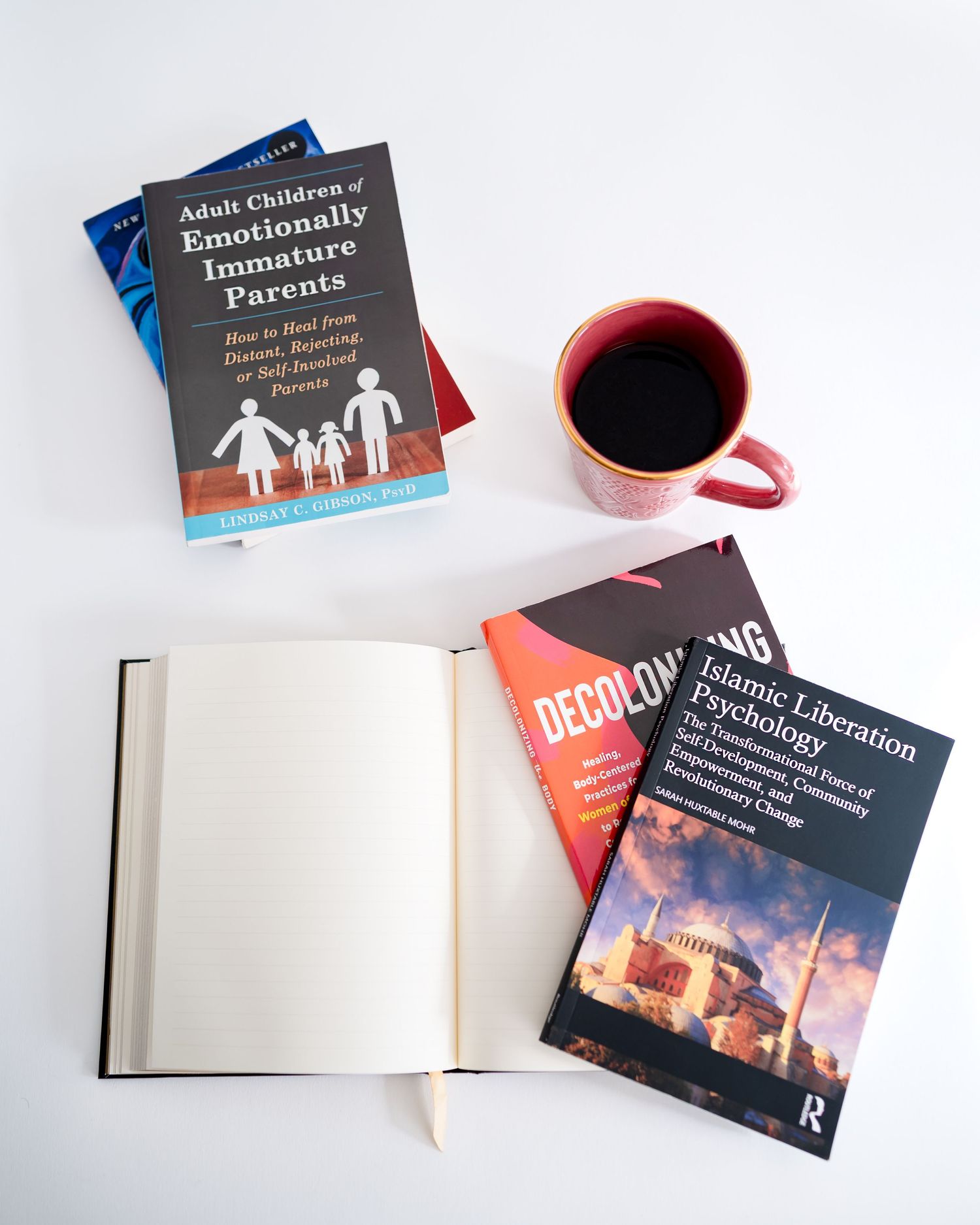 An open hardcover book lies on a white surface with various educational books and a red coffee mug scattered around it.