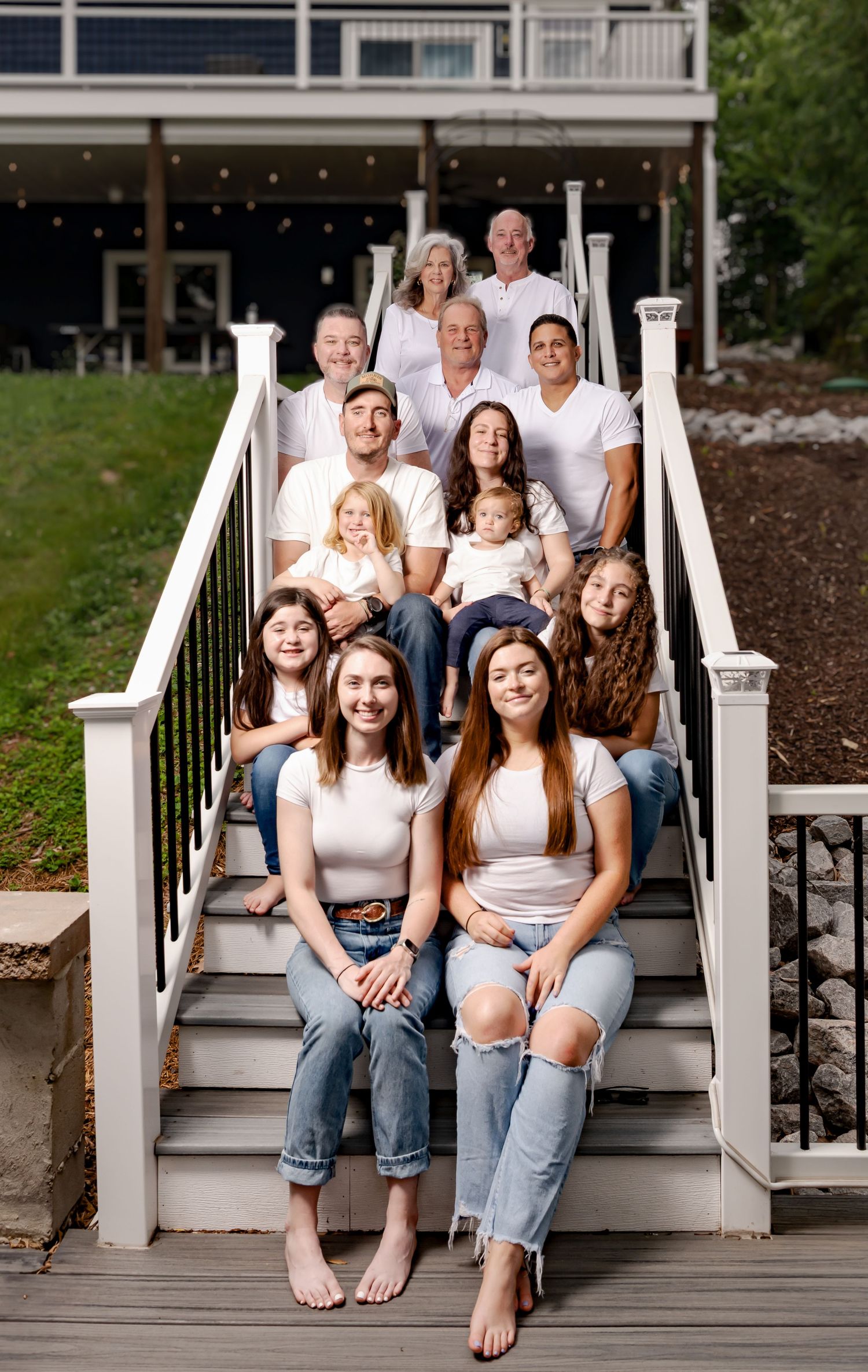Multi-generational family portrait on white porch steps wearing coordinated casual outfits.