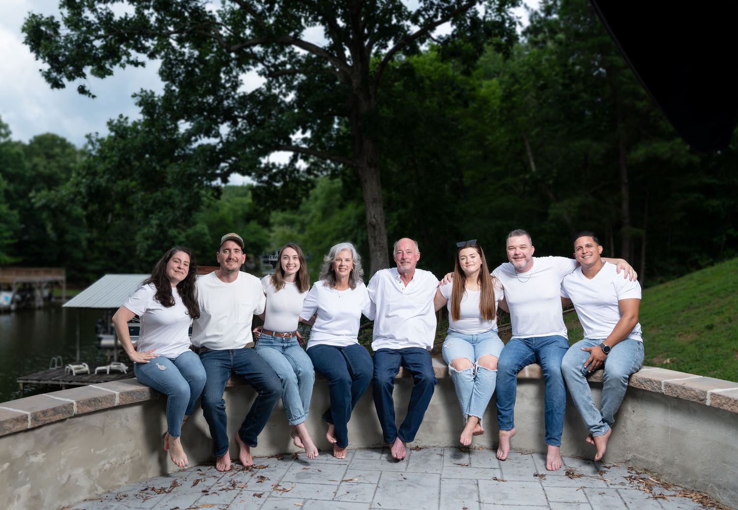 Family group sitting casually on outdoor stone steps wearing white shirts and blue jeans.