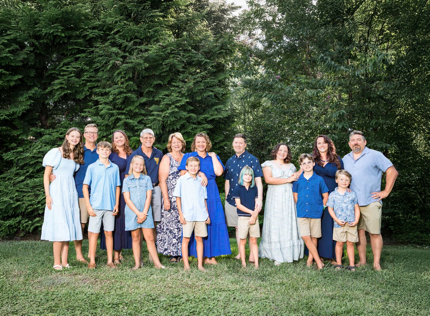 Large group wearing coordinated blue and white outfits poses together for outdoor summer family photo.