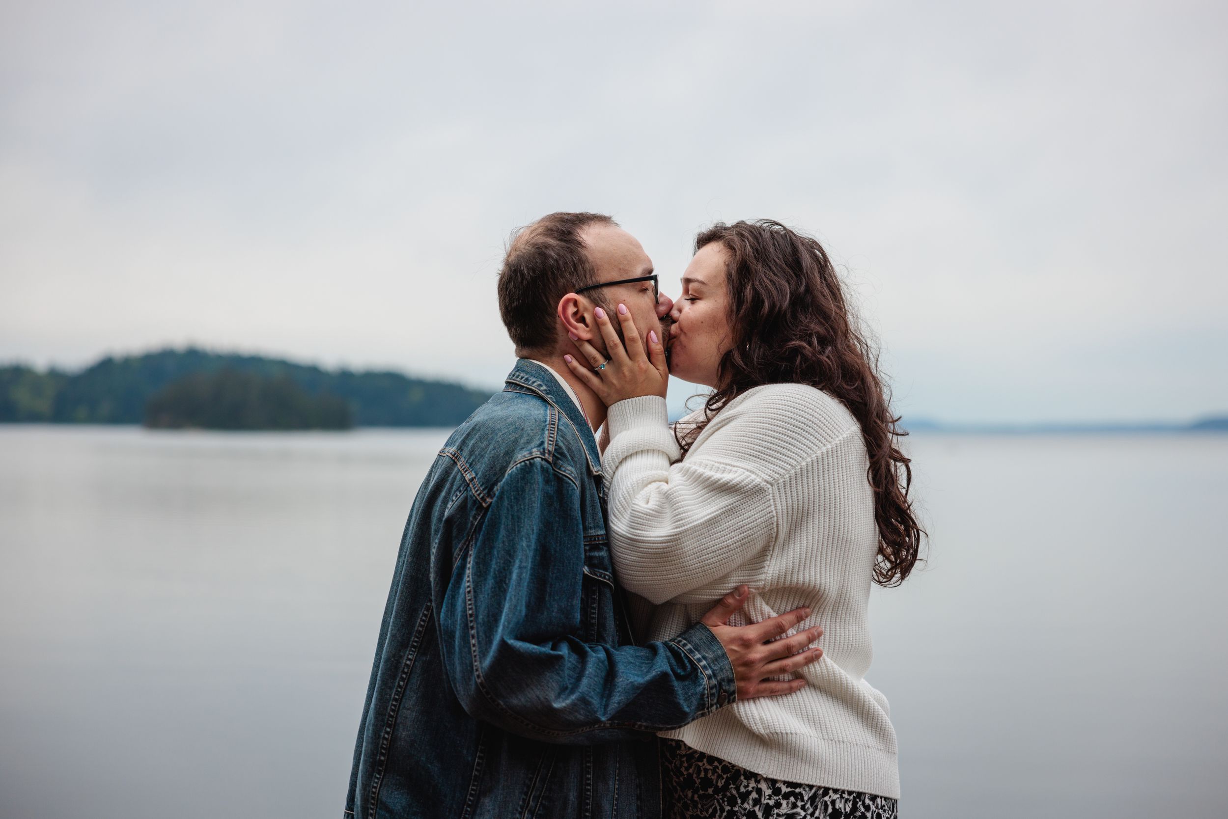 Couple sharing a romantic kiss by a misty lake with forested islands in the background.