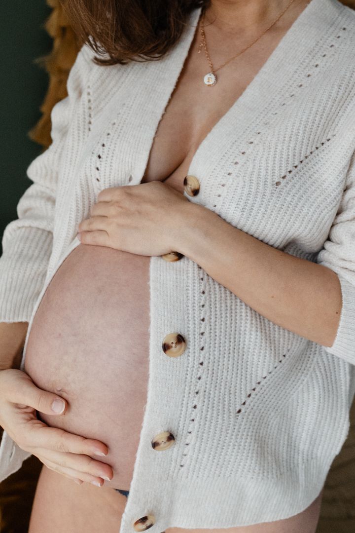 Ventre rond de femme enceinte dont la peau est mise en valeur par la texture d'un gilet en maille lors d'une seance photo grossesse a Lille