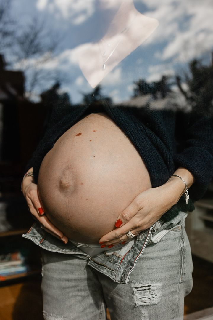 ventre rond d'une femme enceinte a travers une vitre en seance photo grossesse a domicile a Lille avec Nathalie Klein photographe