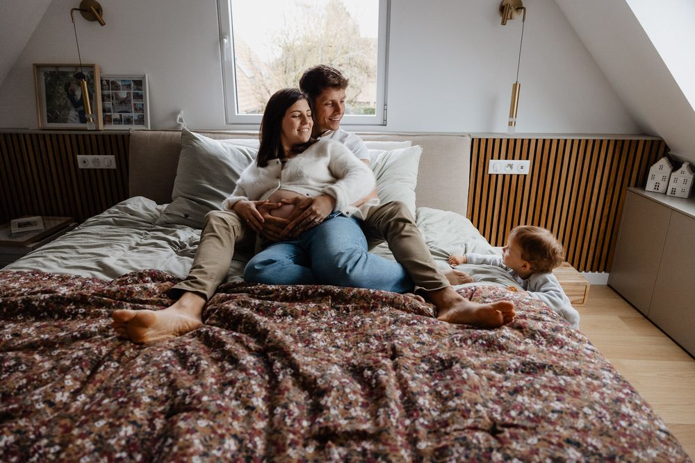 photographe lille : couple de futurs parents se calinant sur le lit pendant que leur fils de un an a peine vient interagir avec eux