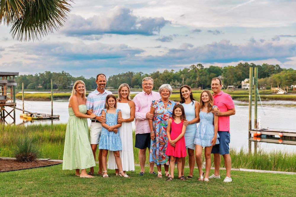 Family gathering poses by coastal marsh with palm trees and boats in background.