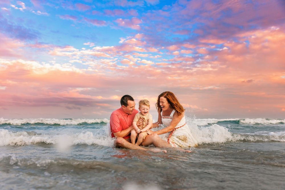 Family plays in ocean waves during vibrant sunset beach photoshoot.