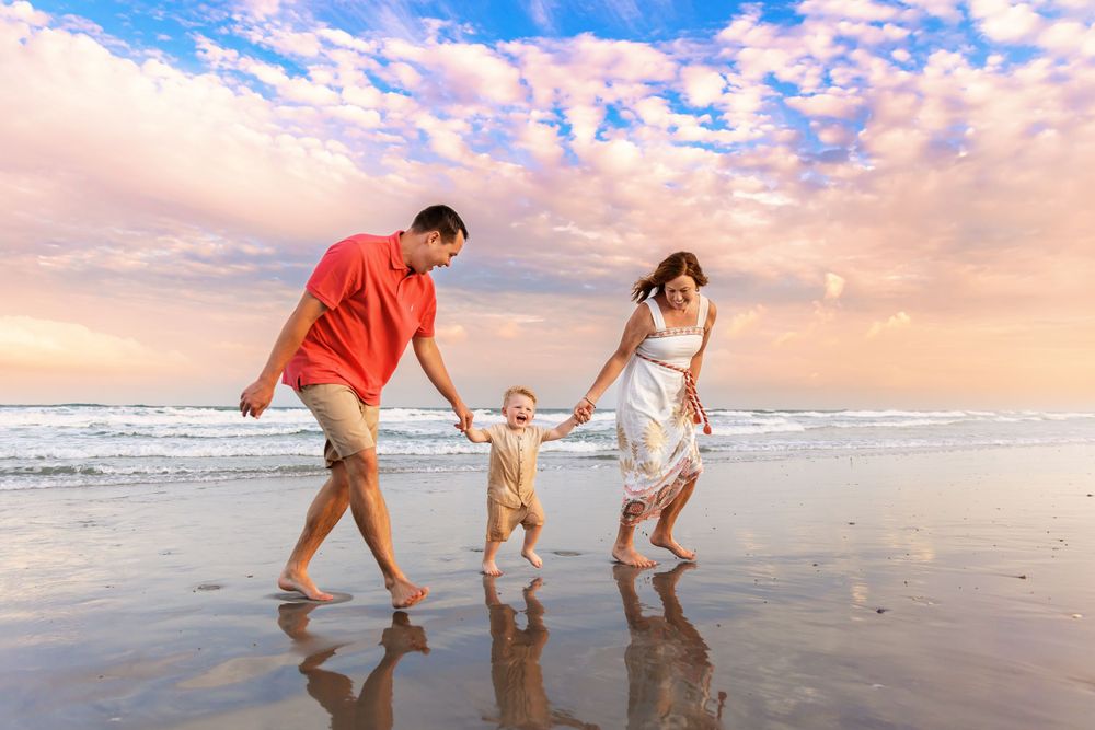 Family walks along beach shore during colorful sunset.