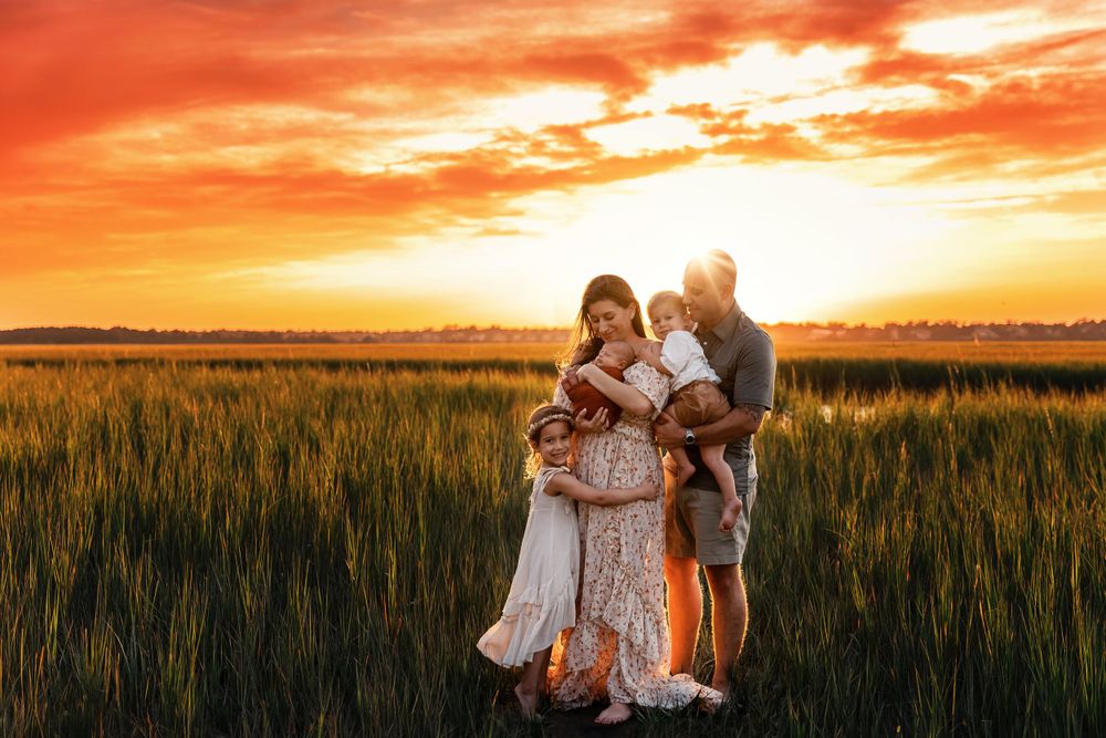 A loving family embraces in a wheat field during a vibrant orange sunset creating a heartwarming silhouette.