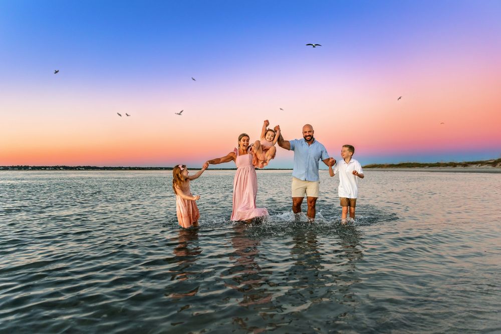 A joyful family plays during sunset at Wrightsville Beach while seabirds fly overhead. Family session captured by Samantha Ann Photography