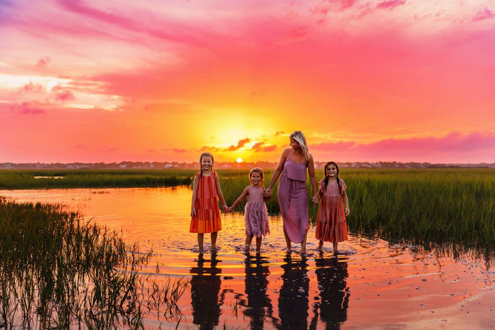 A mother-daughter silhouette against a dramatic orange sunset at the intercostal of Wrightsville Beach captured by Samantha Ann Photography.