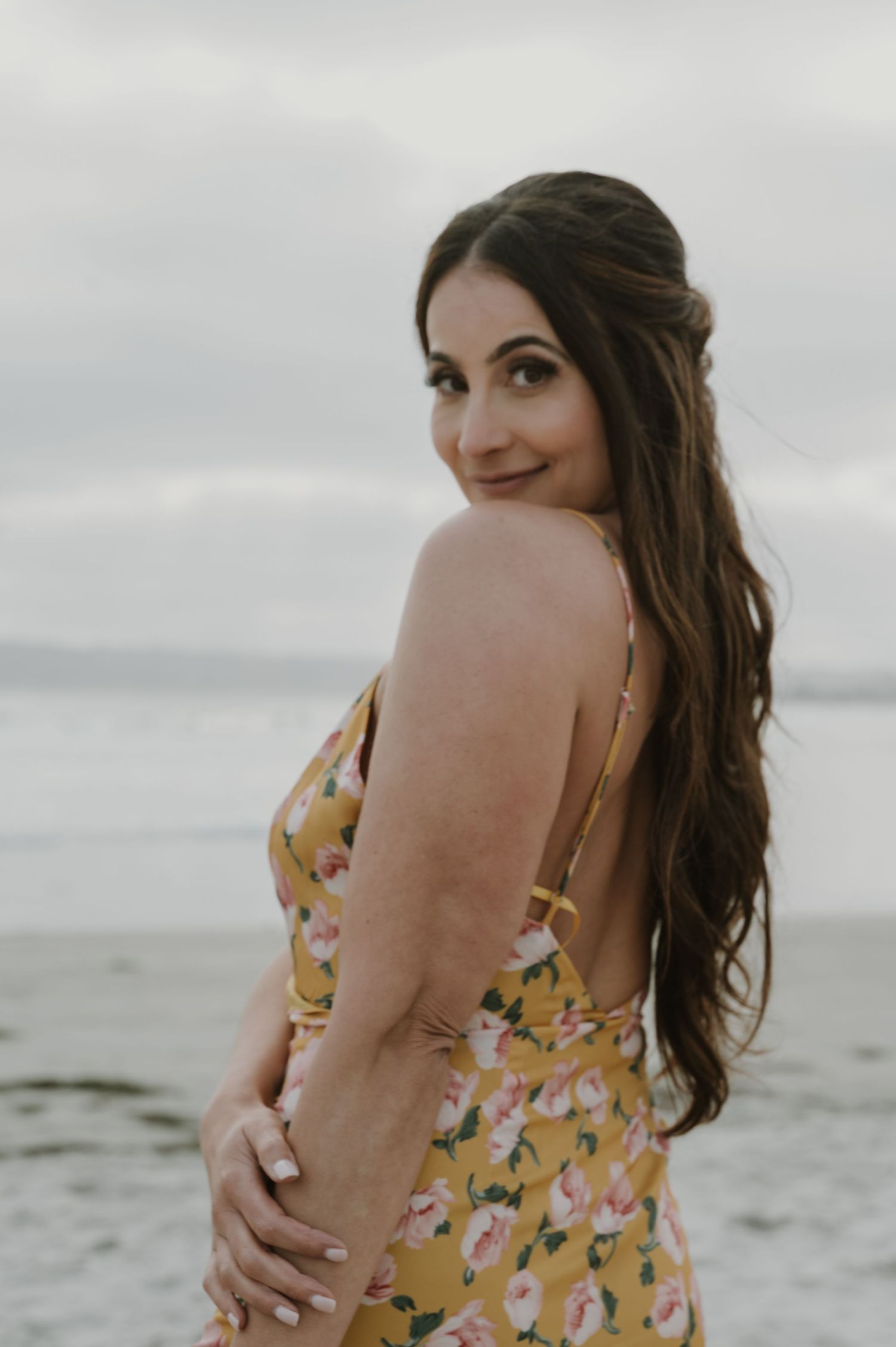 Woman in floral dress poses at beach during golden hour.
