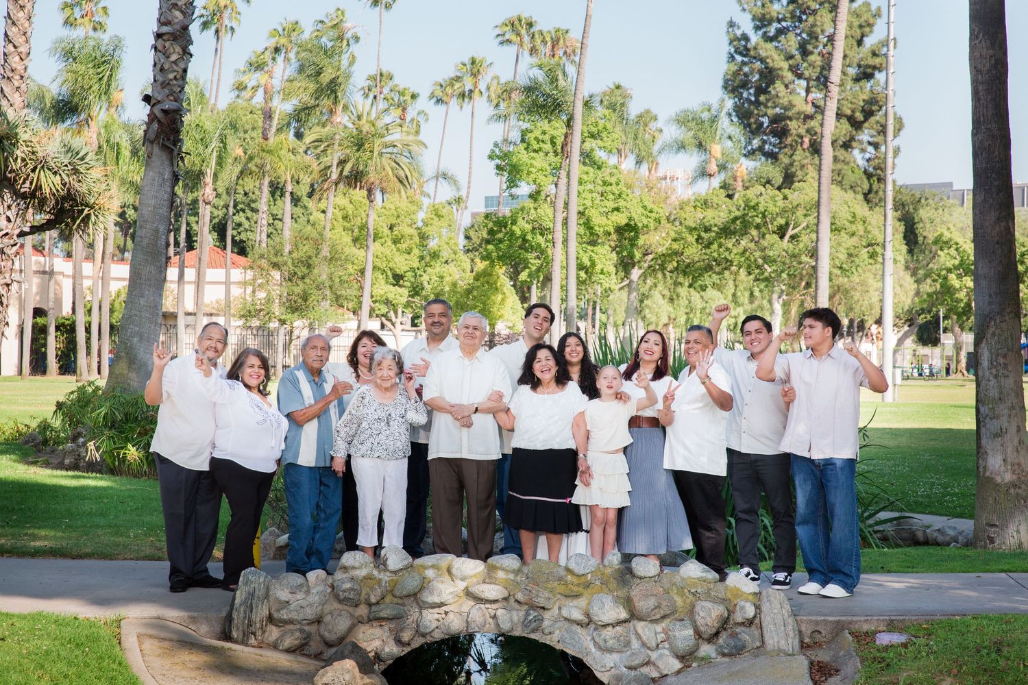 A large group of people in white attire pose together outdoors among palm trees.