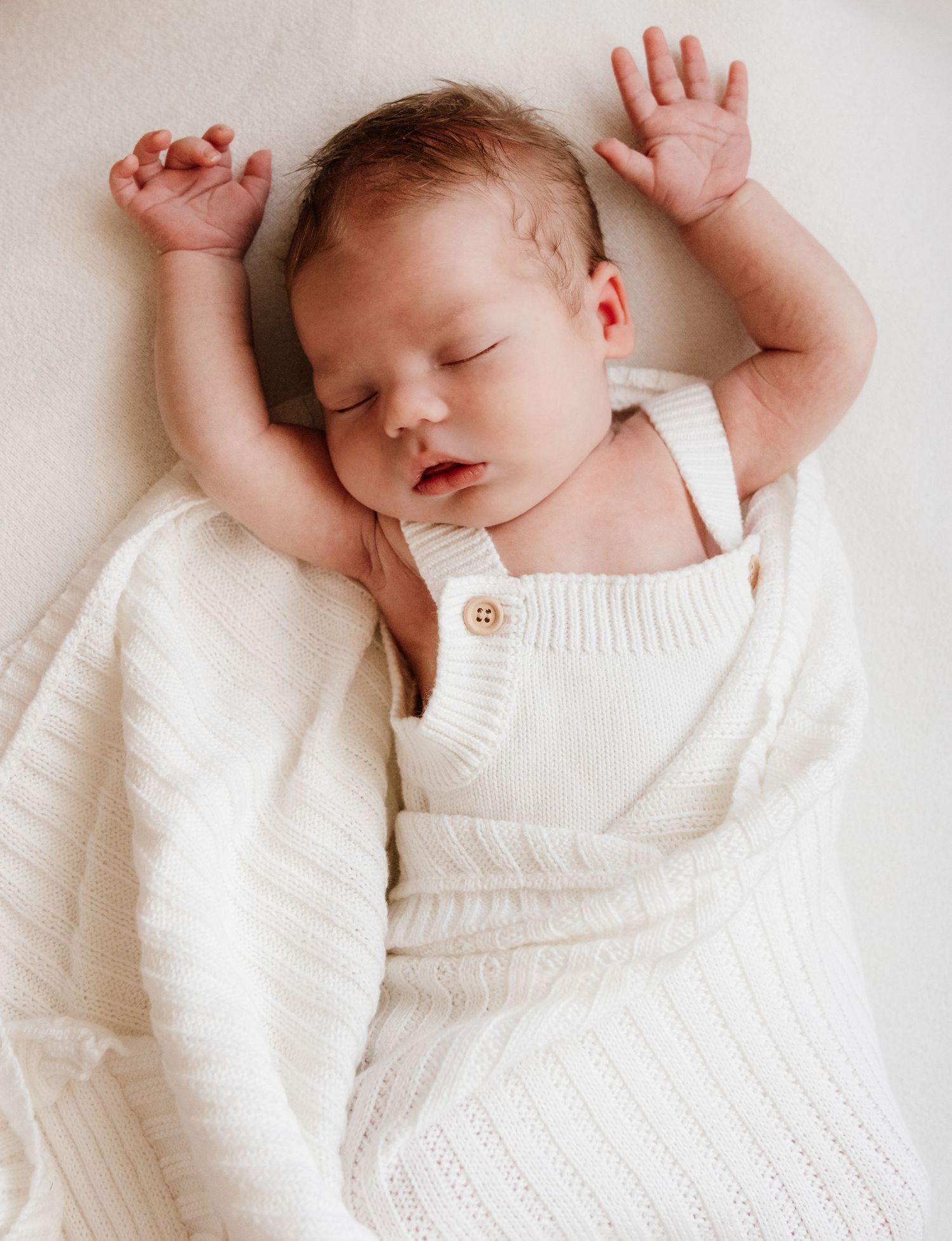 Sleeping newborn baby wearing white knit clothing on white background.
