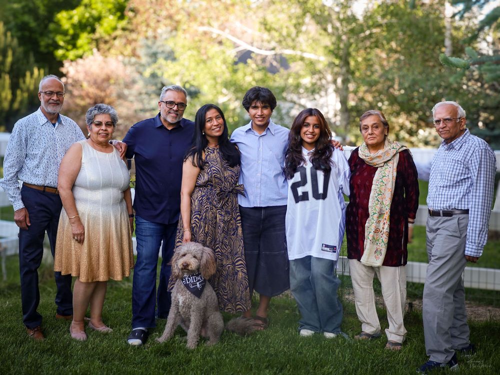 A multi-generational family poses together outdoors with their golden doodle dog on a sunny day.