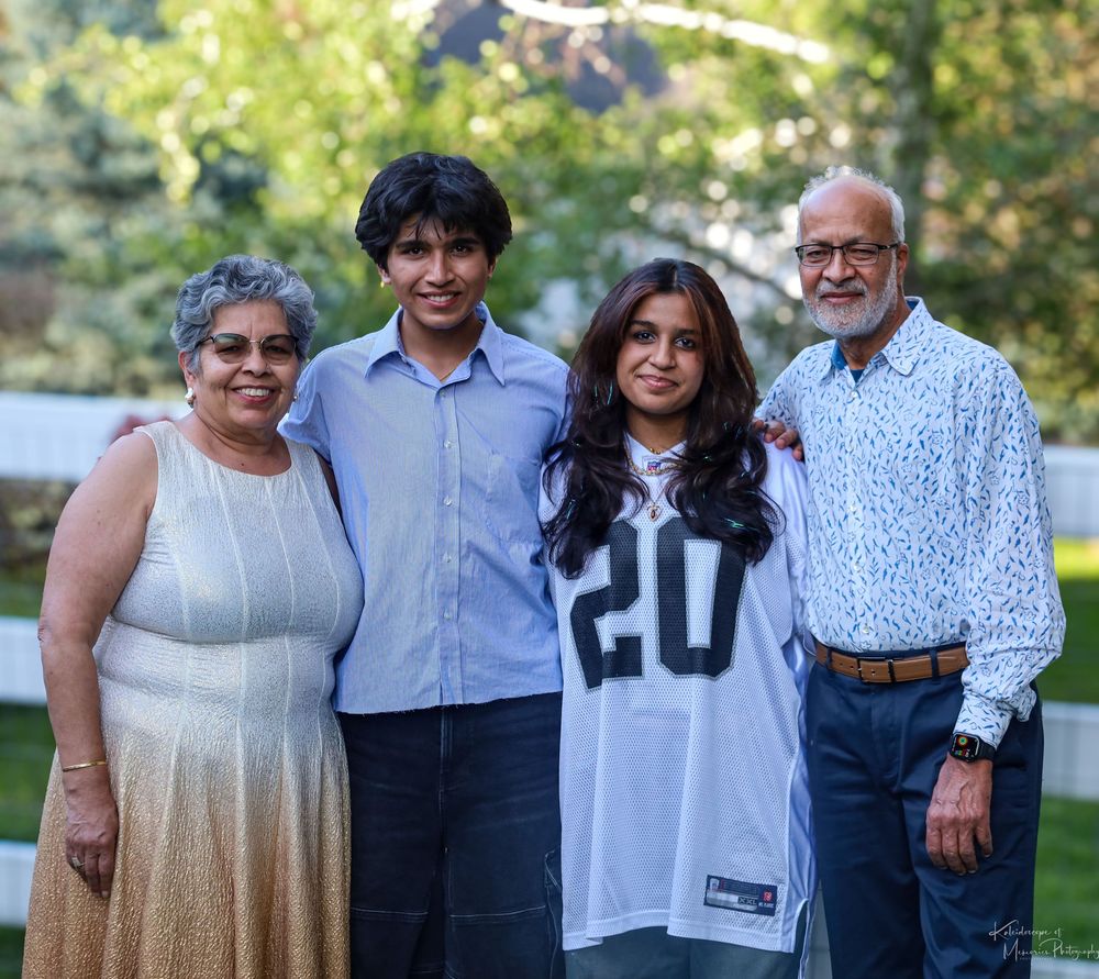 A family of four poses together outdoors, with one member wearing a white sports jersey with number 20.