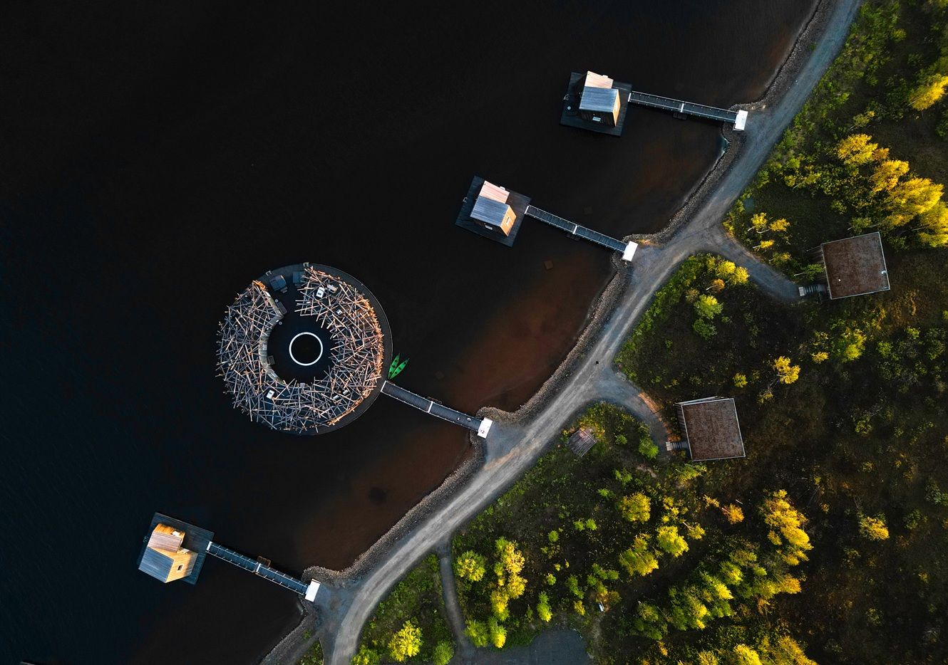 Aerial view of a lakeside resort with circular dock, wooden piers, and autumn trees in Finland.