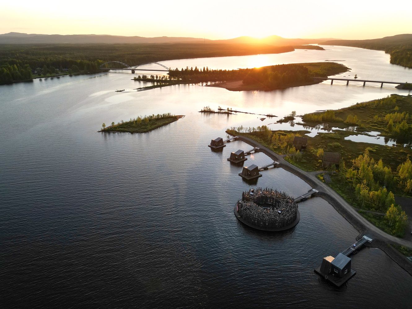 Aerial sunset view of a unique floating resort with nest-like structures on a calm river surrounded by forests.