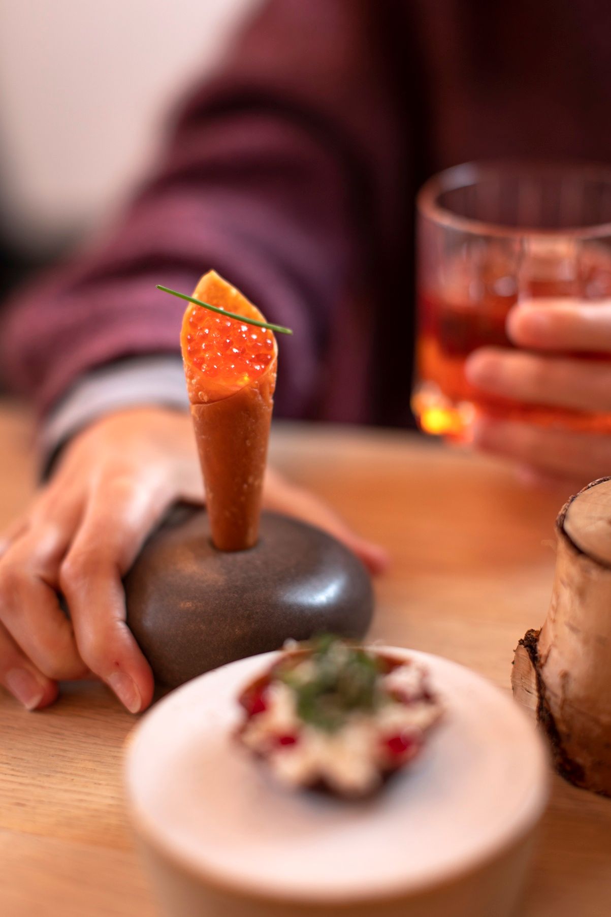 Elegant appetizer cone with salmon roe on stone holder, cocktail and garnished dish at fine dining restaurant.