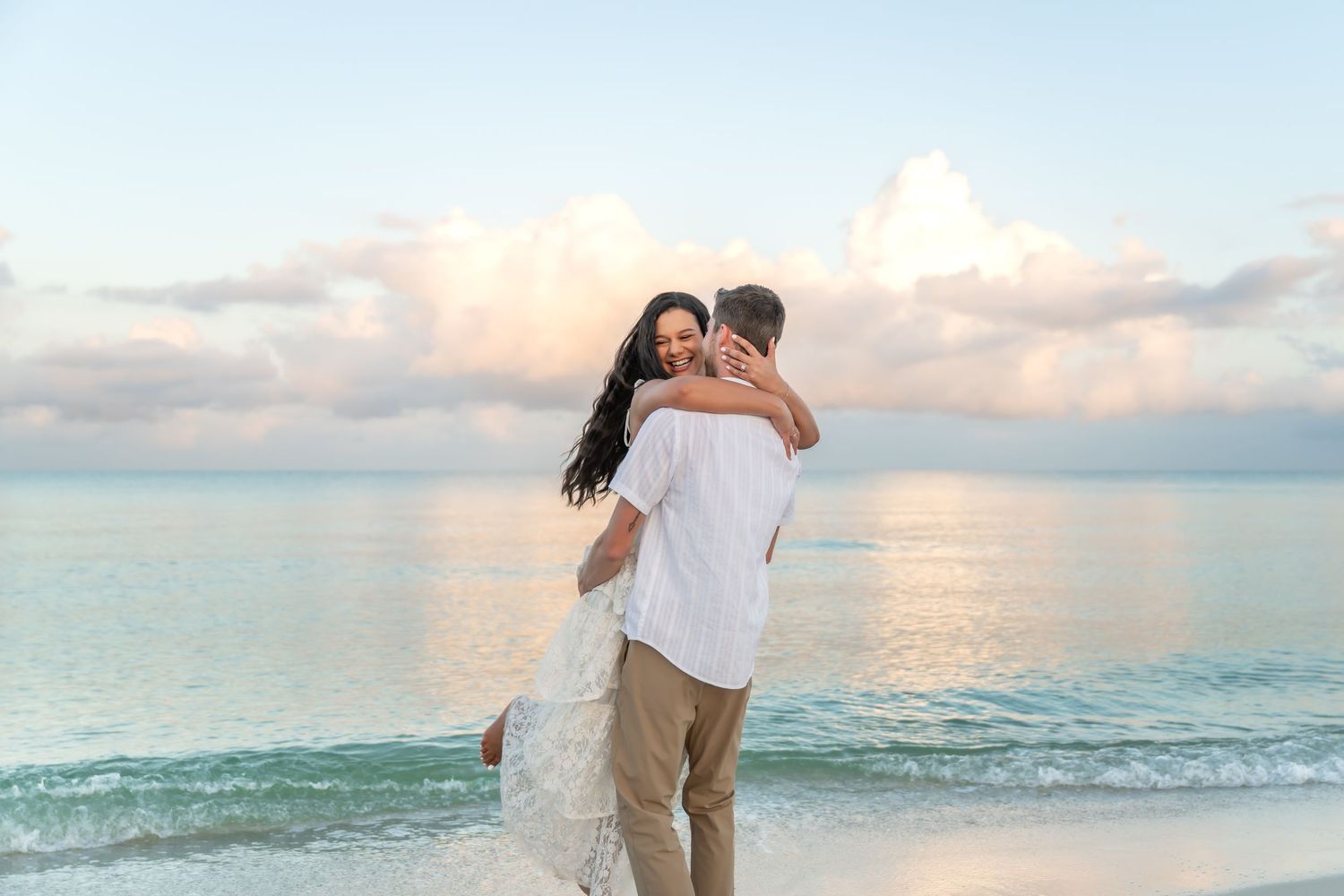 A romantic couple walking and embracing on a pristine beach at sunset with pink and blue pastel sky.