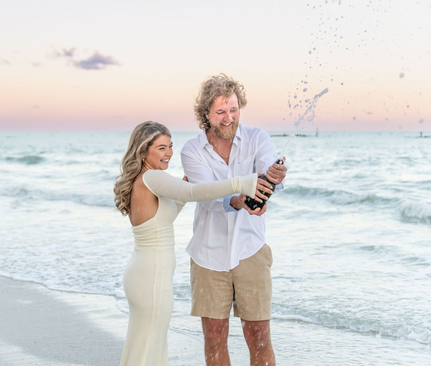 Two people walking together on a sandy beach during sunset while ocean waves roll in behind them.