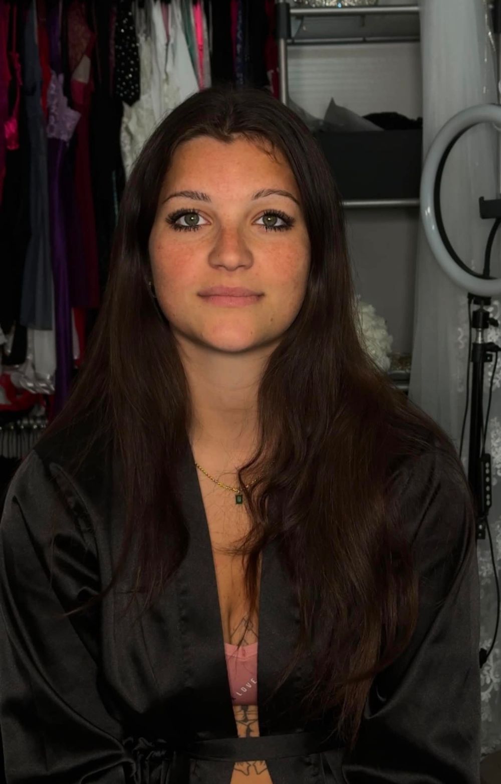 Young woman with long dark hair wearing a black satin robe, posing in front of a clothing rack.