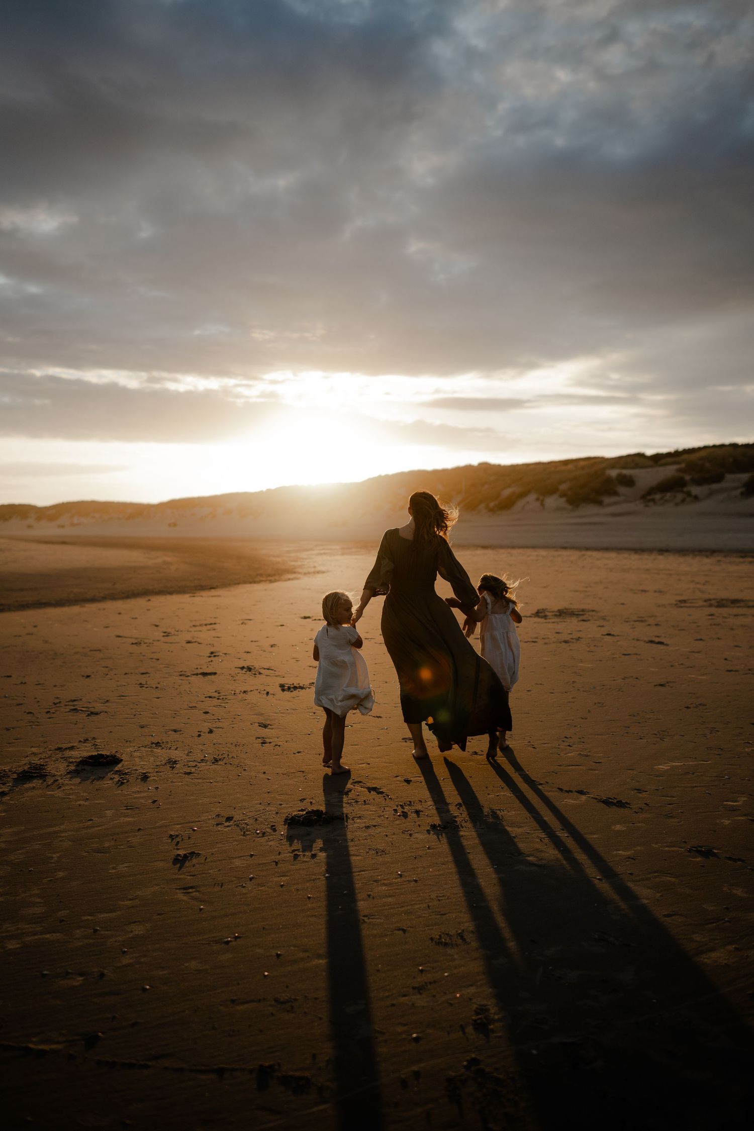A mother running with her daughters on the beach, Kent family photographer
