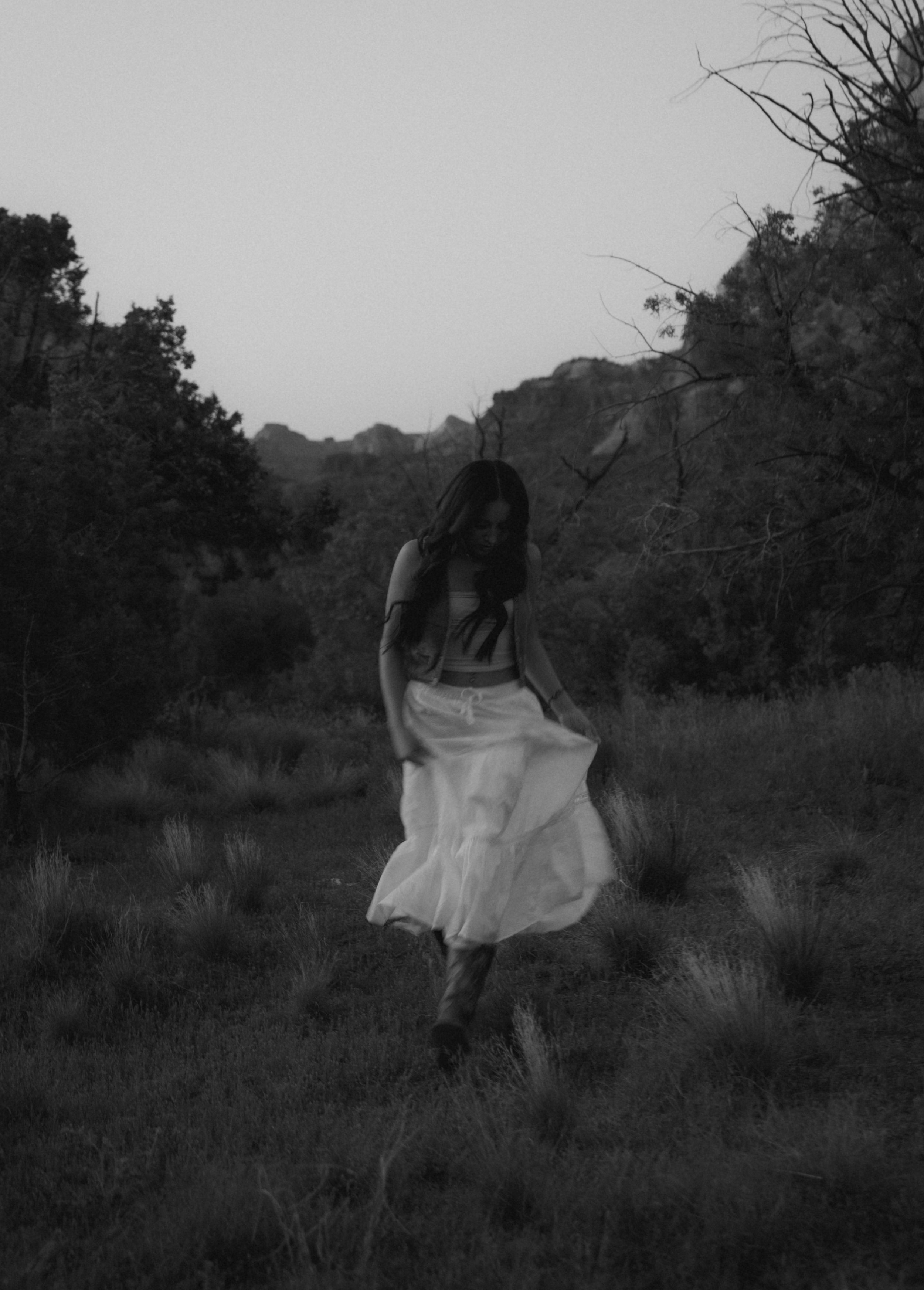 A black and white photo captures someone twirling in a white dress among desert brush.