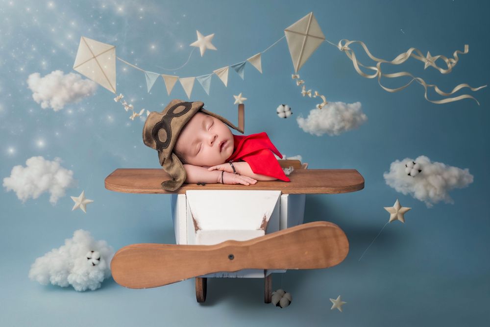 A child in a cardboard airplane prop with paper airplanes and clouds against a dreamy blue backdrop.
