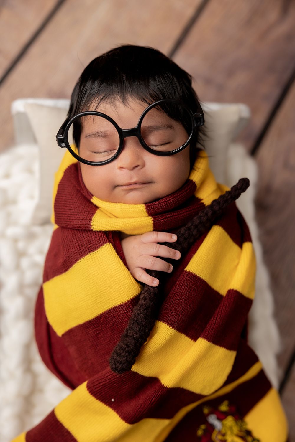 A sleeping baby wrapped in a cozy red and yellow striped scarf and wearing round glasses.