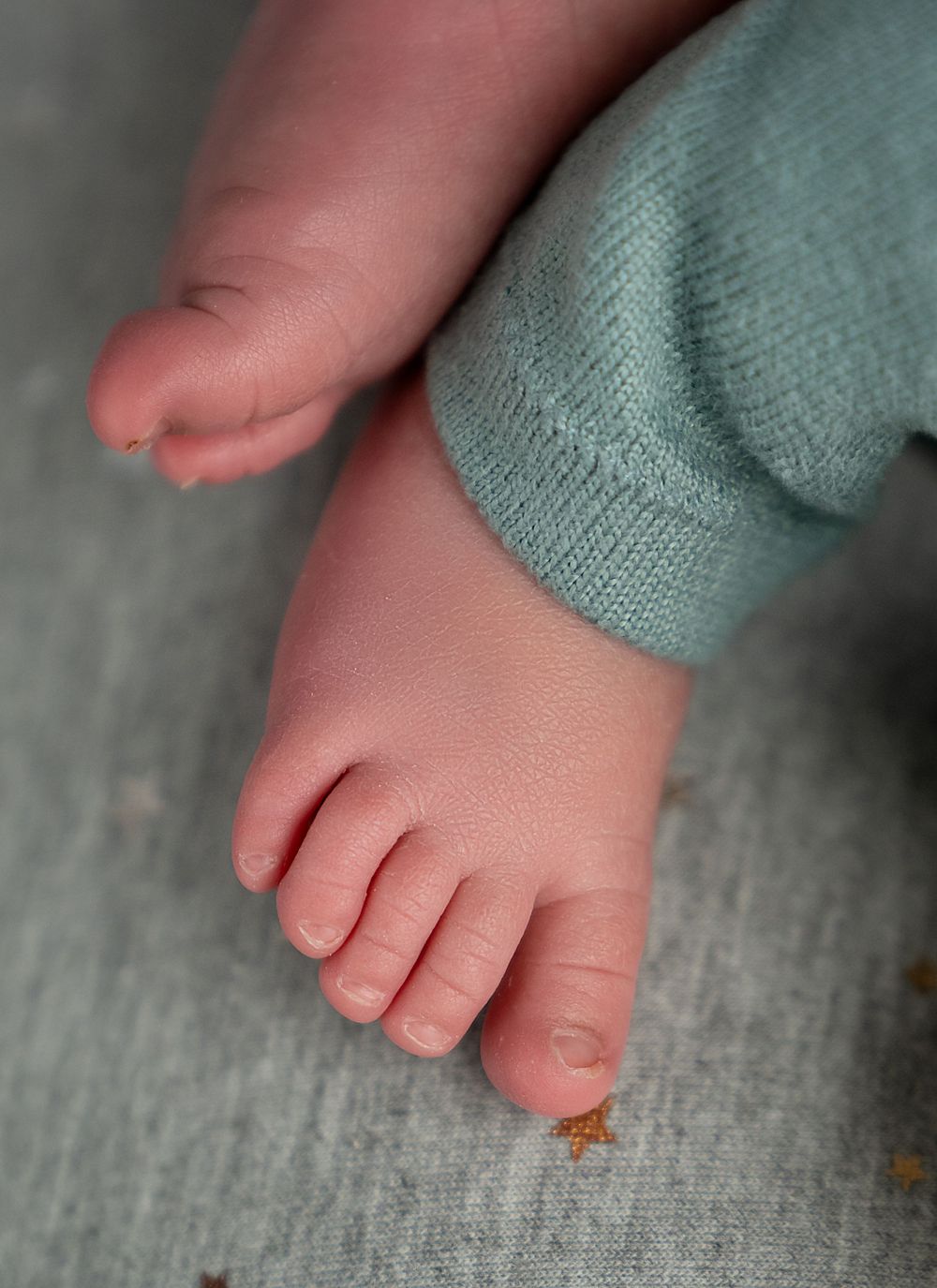 Close-up series showing tiny pink baby toes against a soft gray textured fabric background.