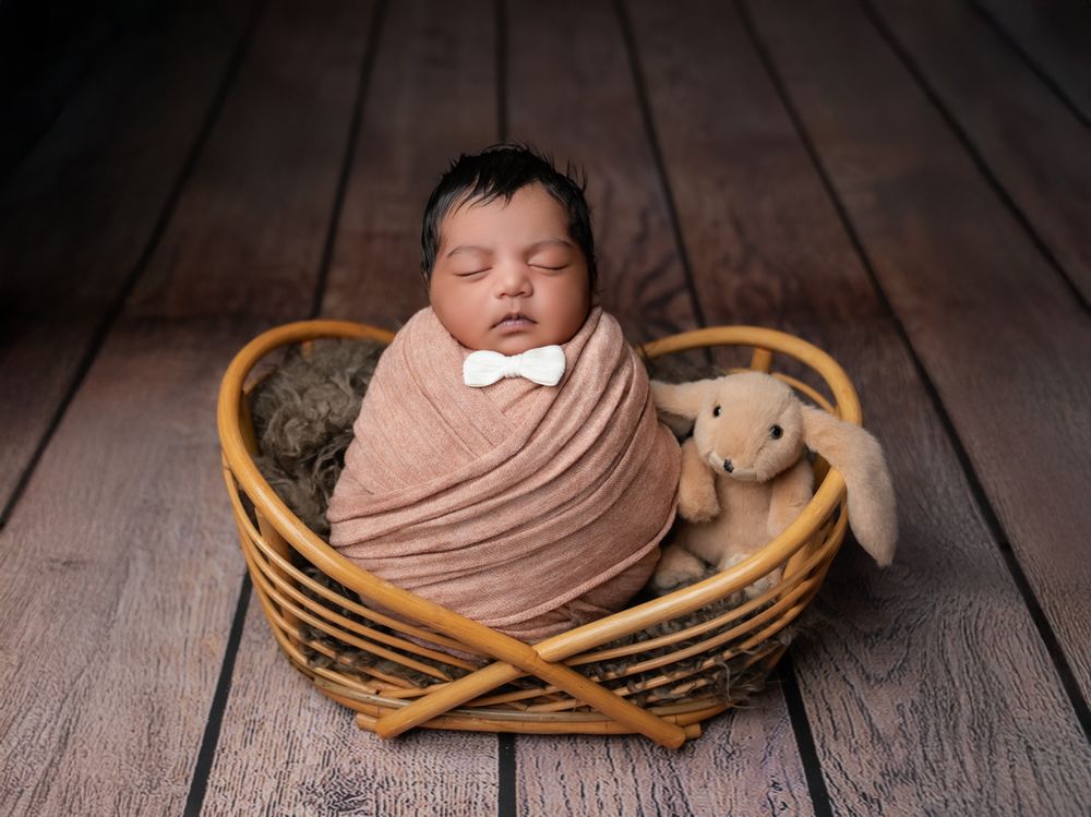 Six sequential photos showing a sleeping newborn baby posed in a wooden basket with soft pink wraps on wooden flooring.