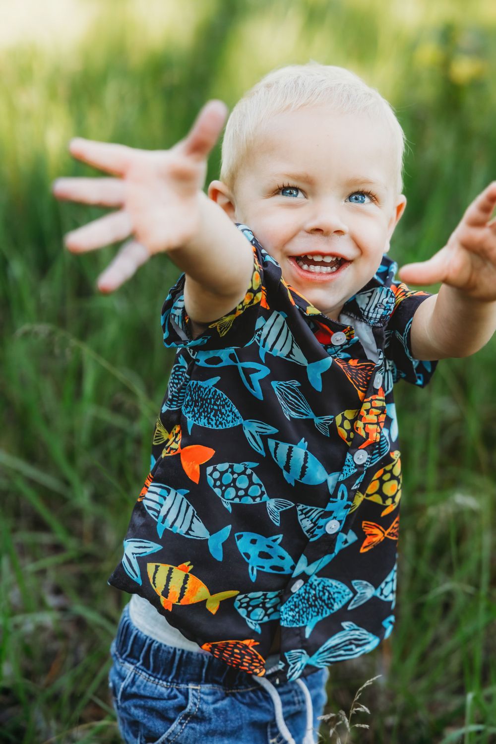 Young child wearing fish print shirt reaches out playfully in green grass.