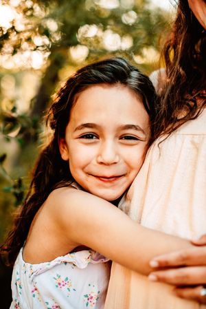 Close up portrait of daughter hugging another mother wearing a floral dress in outdoor setting.
