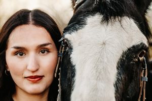 A close-up portrait shows a woman and a black and white horse standing side by side outdoors.
