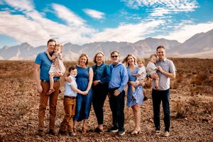 A group stands together for a portrait against a backdrop of majestic mountains on a sunny day with blue skies and clouds.