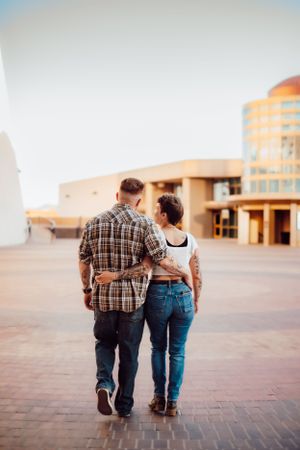 Couple walking together wearing casual clothes at sunset with building in background.