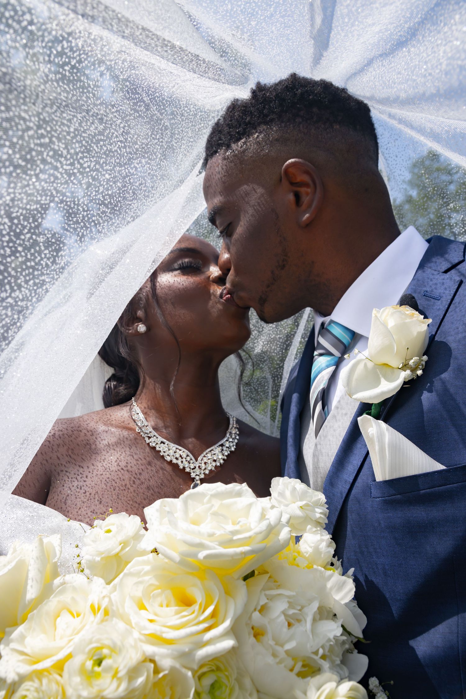 A romantic outdoor wedding ceremony takes place under a white floral arch in a lush garden setting.