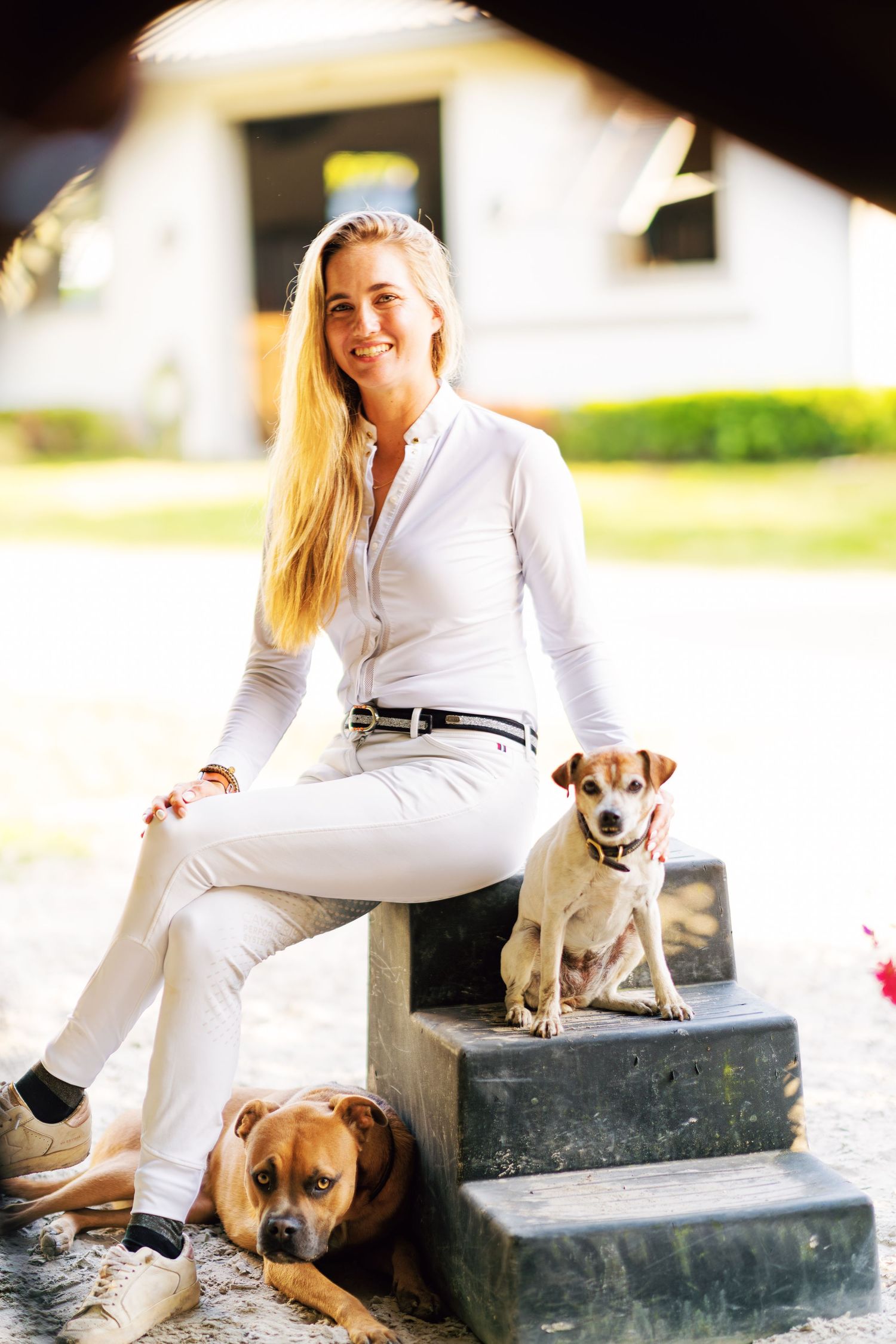 A person in white clothing sits on concrete steps with a small brown dog in a bright outdoor setting.