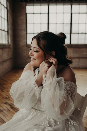 Beautiful off-shoulder wedding dress with sheer puffy sleeves and intricate details shown in a rustic indoor setting.