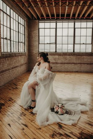 A romantic bridal portrait featuring an elegant white gown with flowing train in a rustic brick loft with large windows.