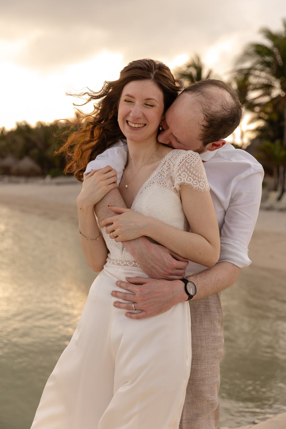 A candid beach portrait of a couple laughing and embracing at sunset with wind-swept hair.