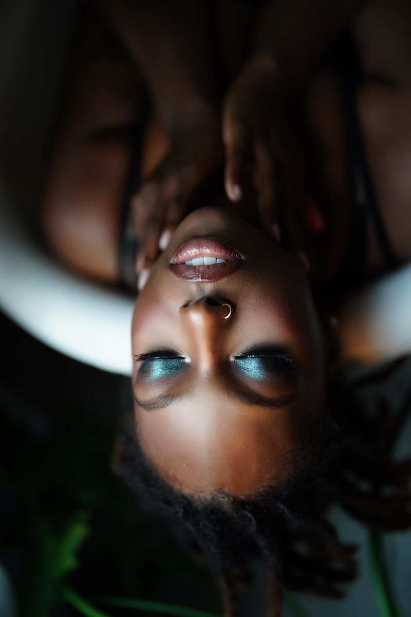 Close-up beauty portrait showing metallic blue eyeshadow and glossy lips with dramatic lighting.